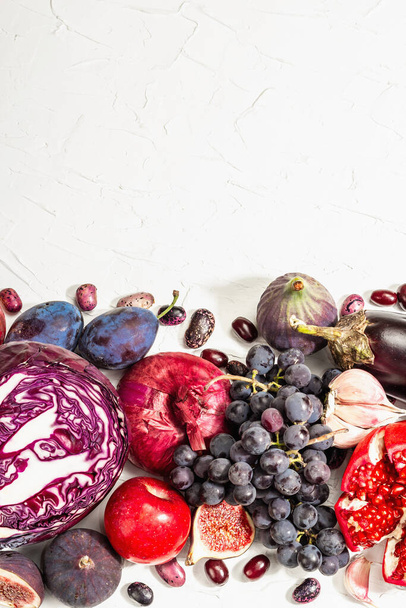 Blaues, rotes und violettes Essen. Kulinarischer Hintergrund von Obst und Gemüse. Frische Feigen, Pflaumen, Zwiebeln, Auberginen, Trauben, Kohl, Äpfel, Knoblauch, Hartriegel, Granatapfel. Weißer Hintergrund, trendiges hartes Licht - Foto, Bild
