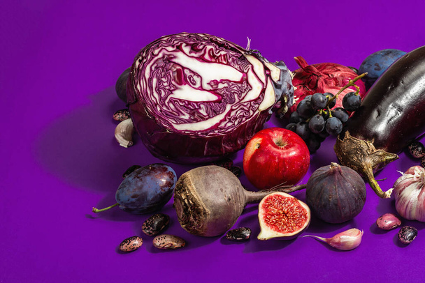Blue, red and purple food. Culinary background of fruits and vegetables. Fresh figs, plums, onions, eggplant, grapes, cabbage, apples, garlic, dogwood, pomegranate. Violet background, trendy hard light - Photo, Image