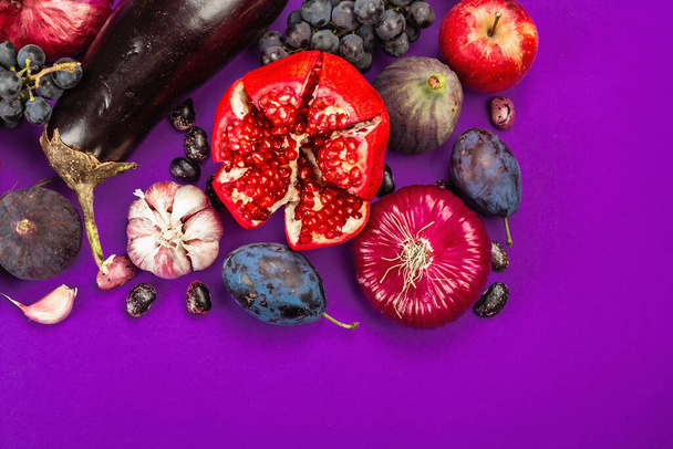 青、赤、紫の食品。果物や野菜の料理の背景。新鮮なイチジク、プラム、タマネギ、ナス、ブドウ、キャベツ、リンゴ、ニンニク、ドッグウッド、ザクロ、ビートルート。バイオレット背景、フラットレイ - 写真・画像