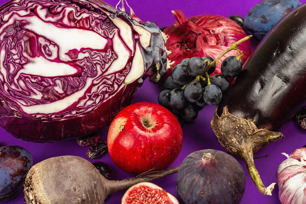 Blue, red and purple food. Culinary background of fruits and vegetables. Fresh figs, plums, onion, eggplant, grapes, cabbage, apple, garlic, dogwood, pomegranate, beetroot. Violet background, flat lay - 写真・画像