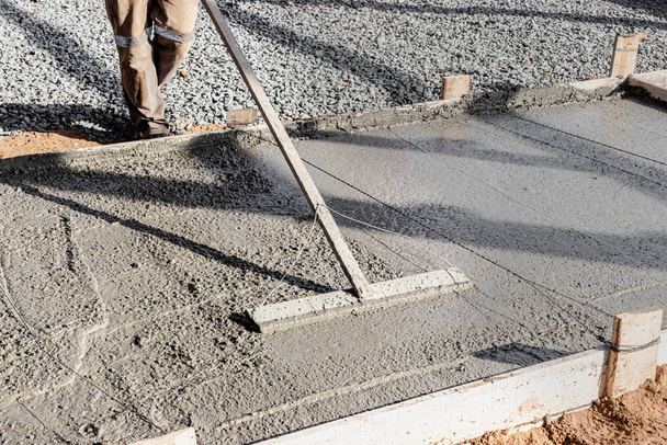 Un ouvrier de la construction termine et aplanit la surface en béton de la fondation sur un chantier de construction - Photo, image