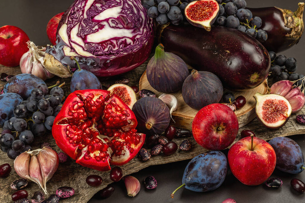 Sinistä, punaista ja violettia ruokaa. Hedelmien ja vihannesten kulinaarinen tausta. Tuoreet viikunat, luumut, sipulit, munakoiso, viinirypäleet, kaali, omenat, valkosipuli, koiruoho, granaattiomena. Musta kivi tausta, tasainen lay - Valokuva, kuva