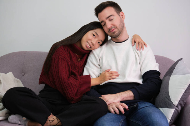 Jeune couple se détendre sur un canapé à la maison en utilisant un ordinateur portable et embrasser. - Photo, image