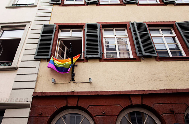 Fasada domu i jego okien z tęczową flagą, symbolem lesbijek, gejów, biseksualistów, transseksualistów (LGBT) i kłirowej dumy oraz ruchów społecznych LGBT, wystających z jednego z okien. - Zdjęcie, obraz