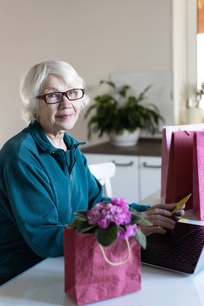 Egy vonzó ősz hajú 85 éves nő vásárol az interneten. Hitelkártyát tart a kezében. Értékesítési koncepció. - Fotó, kép