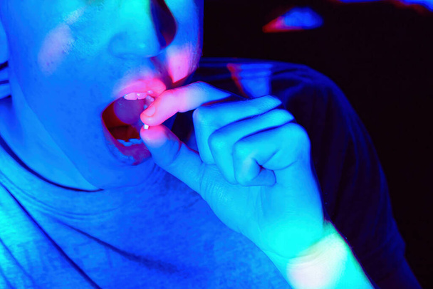 A luz do néon ilumina-se quando um adolescente toma comprimidos de drogas numa discoteca. Conceito de dependência infantil. - Foto, Imagem