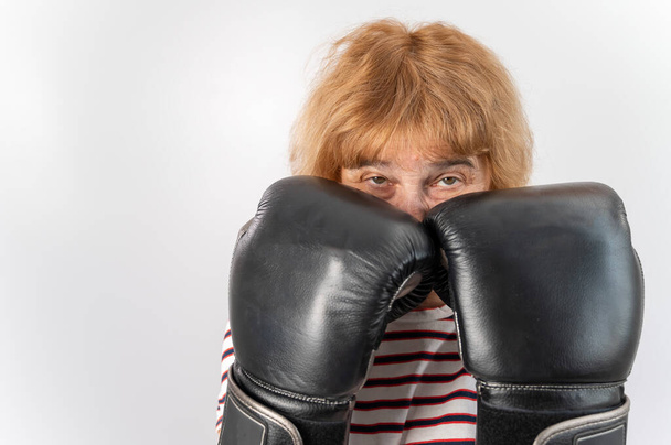 Elderly woman in fighting gloves in a defensive pose on a white background. - Fotó, kép