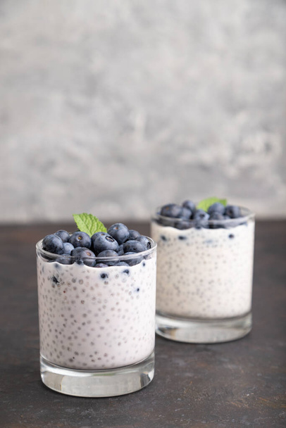 Yogurt with blueberry and chia in glass on black concrete background. Side view, close up, copy space. - Fotoğraf, Görsel