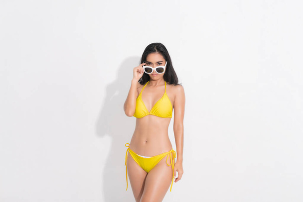 Kaunis nainen onnellisena yllään keltainen bikinit mekko ja tilalla valkoinen aurinkolasit post käsite kesän muoti studio ampua eristetty valkoisella taustalla. - Valokuva, kuva