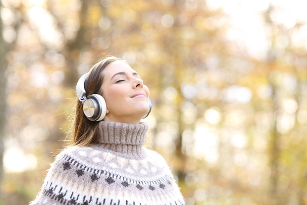 Relaxed woman listening to music and breathing fresh air in autumn in a forest or park - Foto, afbeelding