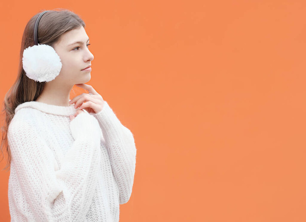  tiener meisje draagt witte oorkappen met trui en staan tegen oranje achtergrond. Een tienermeisje dat opzij kijkt. kopieerruimte. - Foto, afbeelding