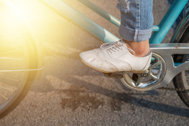 Kobieta w dżinsach i w białych butach jeździ na rowerze po parku - Zdjęcie, obraz