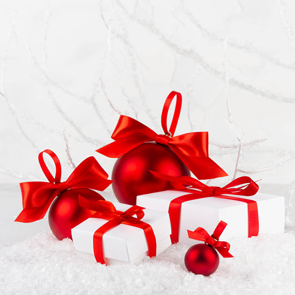 Christmas festive background in white and red color - shimmer balls and gift boxes with satin ribbon closeup in snowdrift under frosty white branches, snow in winter forest, copy space, square. - Photo, image