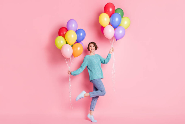 Plná velikost fotografie okouzlující veselá dívka ruce držet balónky zvýšit nohu zubatý úsměv izolované na růžové barevné pozadí - Fotografie, Obrázek
