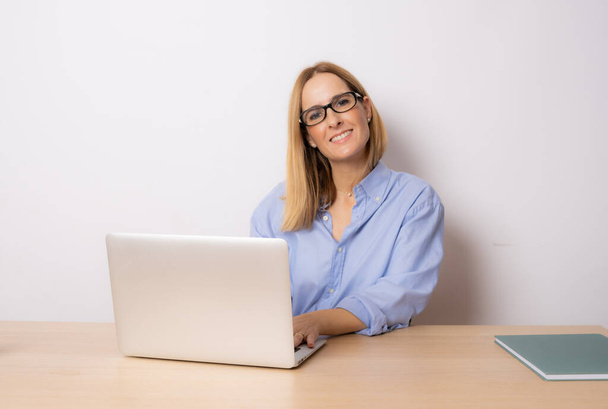 Çekici, neşeli, genç iş kadını dizüstü bilgisayarda çalışıyor ve masasında tek başına otururken gülümsüyor.. - Fotoğraf, Görsel
