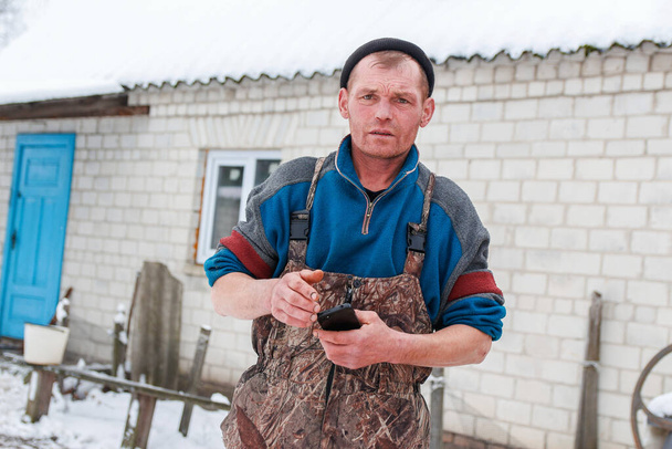 Russian young man standing outside on winter countryside background. Construction worker holding phone. Caucasian laborer man 40 years old, portrait. Poverty concept. Unhappy sad people. - Photo, image
