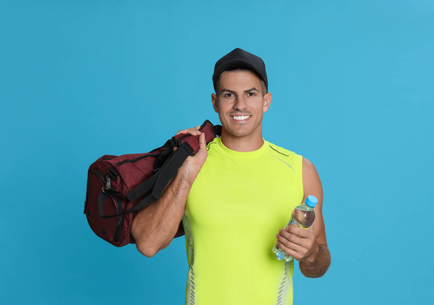 Handsome man with sports bag and bottle of water on light blue background - Foto, Imagen