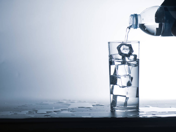 Mensen gieten water uit een fles in een glas schoon drinkwater met ijs. Gezond drinkwaterconcept - Foto, afbeelding