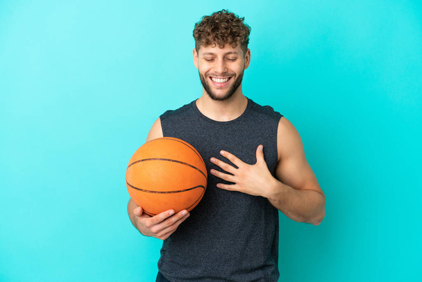 Bonito jovem jogando basquete isolado no fundo azul sorrindo muito - Foto, Imagem