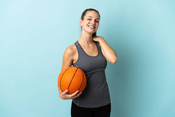 jonge vrouw spelen basketbal geïsoleerd op blauwe achtergrond lachen - Foto, afbeelding