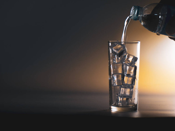 Les gens versent l'eau d'une bouteille dans un verre d'eau potable propre avec de la glace. Concept d'eau potable saine - Photo, image