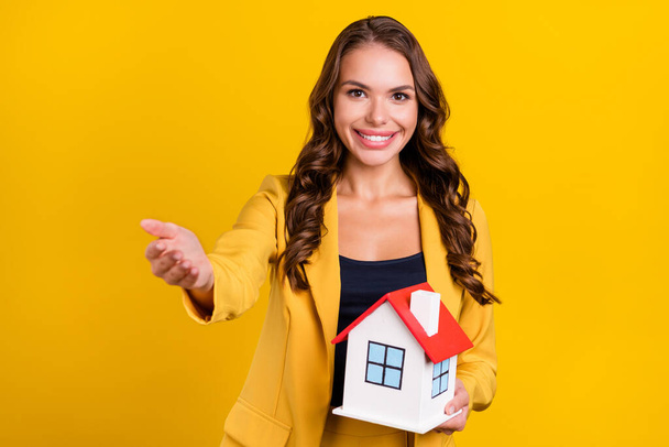Photo of shiny beautiful young lady wear suit jacket inviting you holding arms hands small house smiling isolated yellow color background - Photo, Image