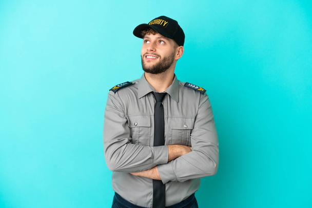 Young security man isolated on blue background looking up while smiling - Photo, image
