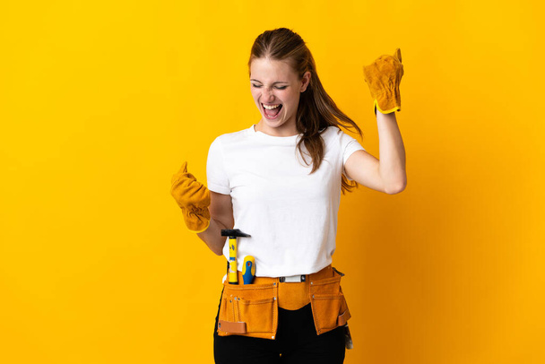 Sarı arka planda izole edilmiş genç elektrikçi kadın zaferi kutluyor. - Fotoğraf, Görsel
