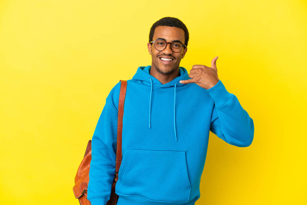Ein afroamerikanischer Student vor isoliertem gelben Hintergrund macht eine Handygeste. Rufen Sie mich zurück - Foto, Bild