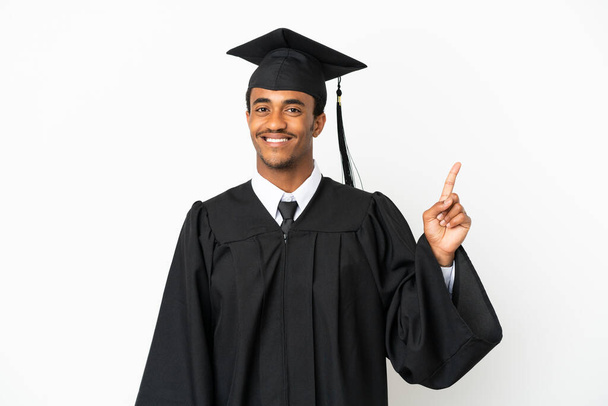 Αφροαμερικανός απόφοιτος πανεπιστημίου πάνω από απομονωμένο λευκό φόντο δείχνει και να άρει ένα δάχτυλο σε ένδειξη του καλύτερου - Φωτογραφία, εικόνα