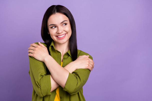 Photo of adorable pretty lady dressed green clothes smiling embracing herself looking empty space isolated purple color background - 写真・画像