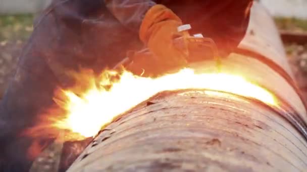 Ένας συγκολλητής σε προστατευτική ενδυμασία στην ύπαιθρο κόβει μεταλλικούς σωλήνες με συγκόλληση ακετυλενίου και φωτιά και σπινθήρες είναι ορατοί. - Πλάνα, βίντεο