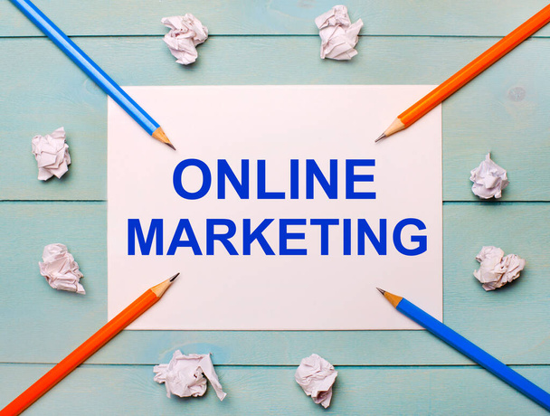 On a blue background - black and orange pencils, white crumpled sheets of paper and a white sheet of paper with the text ONLINE MARKETING - Foto, Imagen