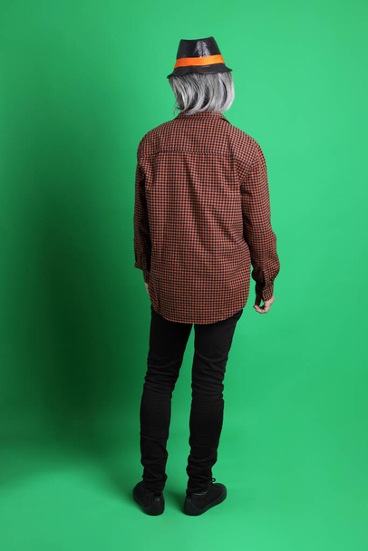 The senior Asian man dressing in Thanksgiving season color theme, wearing orange plaid shirt and black hat standing on the green background. - Foto, immagini
