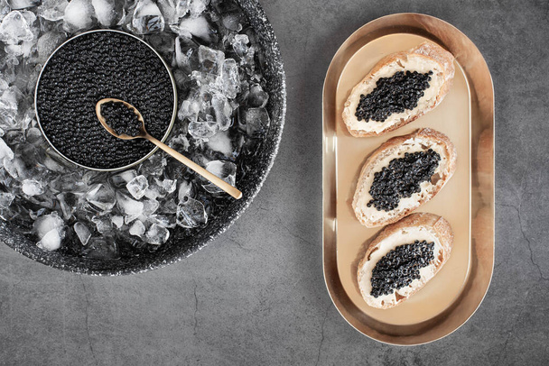 Black caviar in can on ice and bread with butter on golden plate. High quality photo - Zdjęcie, obraz