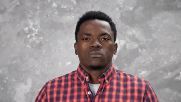 Adulto afroamericano uomo in cerca di fotocamera, in piedi su sfondo grigio muro - Filmati, video