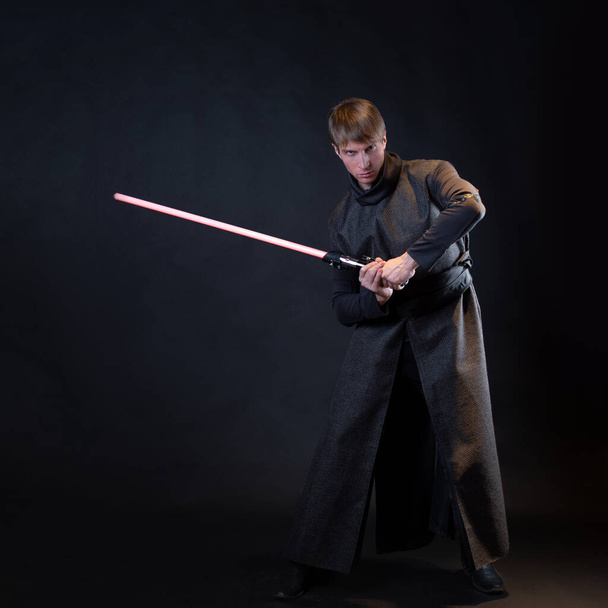 A villain with a red lightsaber, a young man in a long robe does fighting poses, - Foto, Imagen
