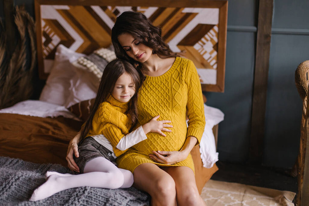 Child hugs mom's pregnant belly. Happy parenting. Expectation of the second child. The sister is waiting for her brother. Siblings. Eco parenting. Cozy boho country interior. Mothers Day - Фото, зображення
