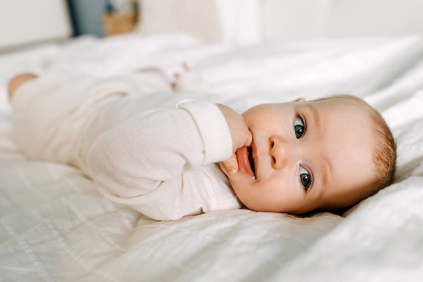Großaufnahme eines glücklichen Babys, das im Bett liegt, lächelt und Finger lutscht. - Foto, Bild