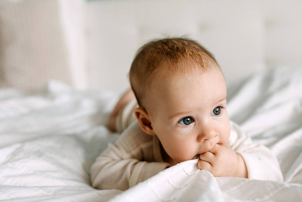 Detailní záběr dítěte ležícího v posteli na břiše, žvýkajícího bílou prostěradlo. - Fotografie, Obrázek
