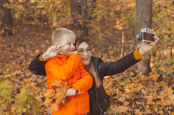 Son and mother are taking selfie on camera in autumn park. Single parent, leisure and fall season concept. - Foto, Bild
