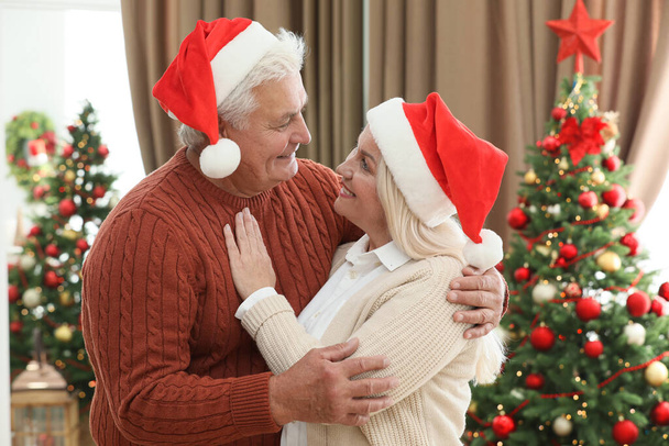 Happy mature couple in Santa hats at home. Christmas celebration - Fotoğraf, Görsel
