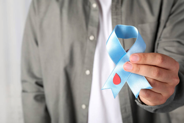 Man holding light blue ribbon with paper blood drop indoors, closeup. World Diabetes Day - Fotografie, Obrázek