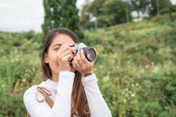 Atractiva mujer asiática tomando fotos con cámara de película retro entre la naturaleza en el campo por la mañana - Foto, Imagen