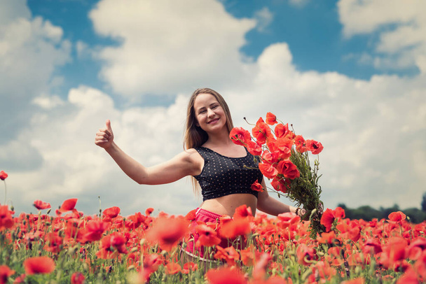 Ukrainian girl in sportwear holding a bouquet of poppies in field, summer time - Photo, Image