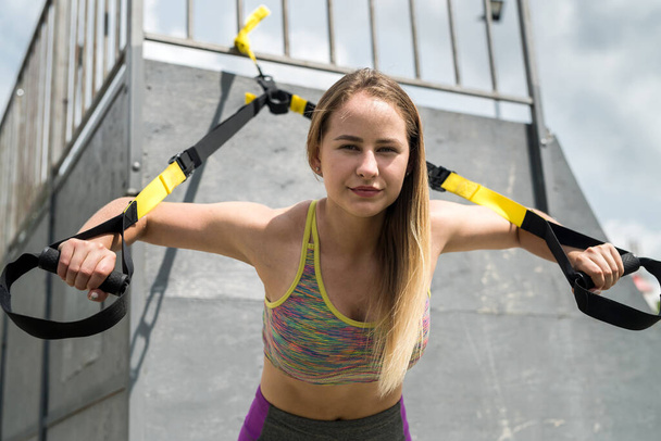 Jeune belle femme en vêtements de sport faisant push-ups bras d'entraînement avec trx sangles de fitness à la nature. Mode de vie sain - Photo, image