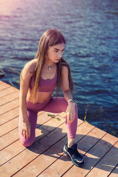 Beautiful young slim woman doing yoga or stretching exercise by the lake. Healthy lifestyle. - Foto, Imagen