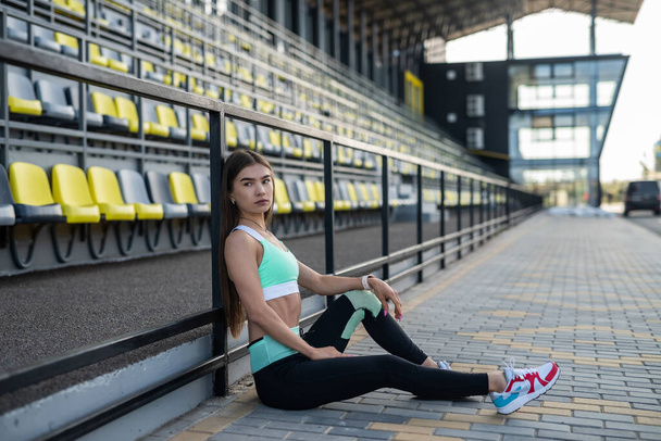mooi sportief meisje hebben rust in de buurt op zit op het stadion in zonnige dag - Foto, afbeelding