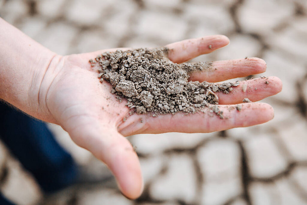 The man is holding the very dry soil in his palm. Concept of soil erosion due to lack of precipitation due to global warming. - Photo, Image