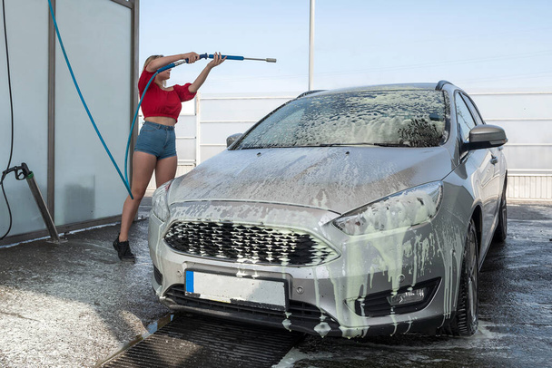 jeune conducteur femme d'un tuyau haute pression applique de la mousse de savon sur la voiture pour le nettoyage de la saleté au lavage manuel de la voiture - Photo, image